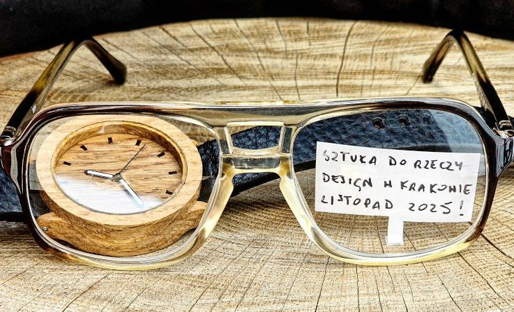 Drewniany zegarek leży na drewnianym stoliku. Przed nim leżą okulary.